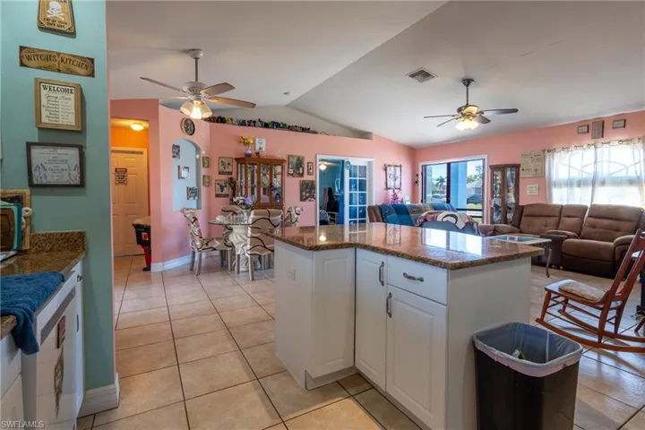 Kitchen with visible vents, a center island, vaulted ceiling, white cabinetry, and light tile patterned flooring
