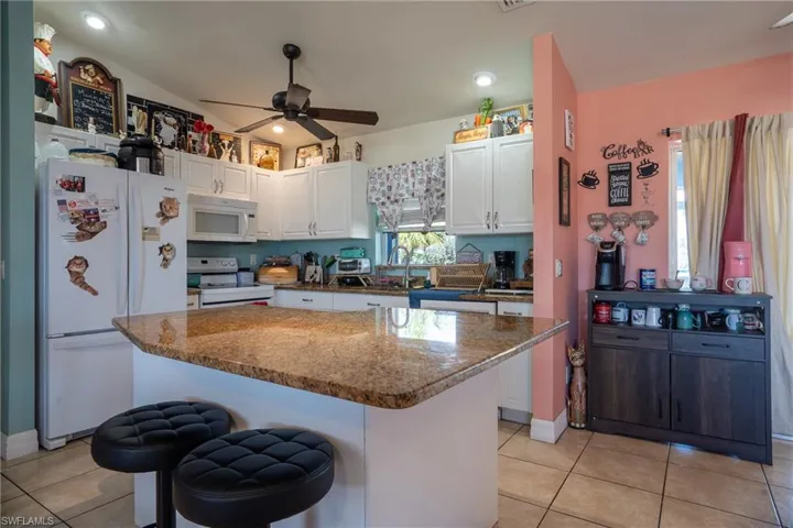 Kitchen with lofted ceiling, white appliances, white cabinetry, and dark stone countertops