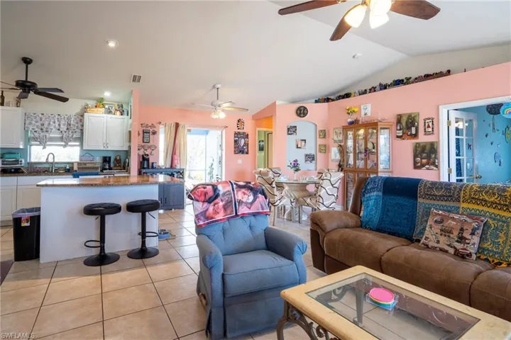Living area with vaulted ceiling, visible vents, light tile patterned flooring, and a wealth of natural light