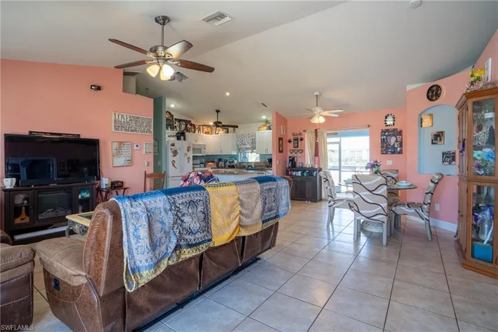 Living area featuring light tile patterned floors, visible vents, vaulted ceiling, and a ceiling fan
