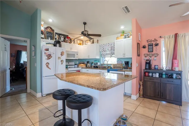 Kitchen featuring white appliances, visible vents, a breakfast bar area, and white cabinetry