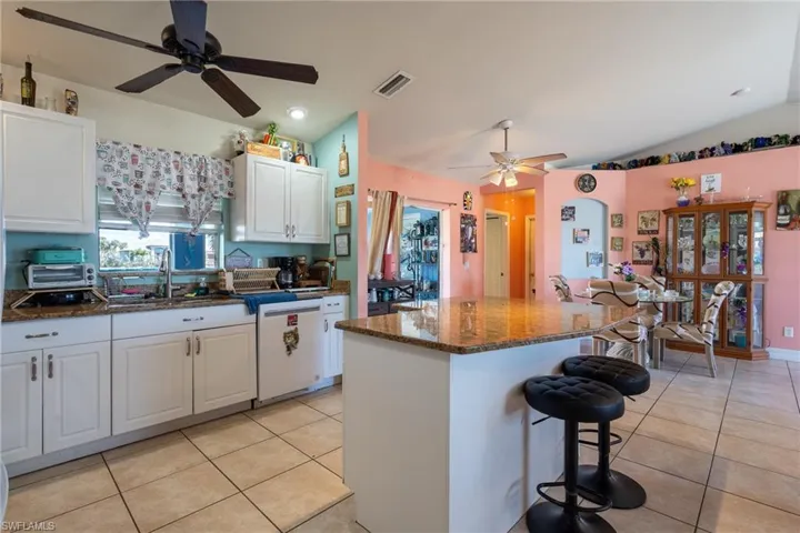 Kitchen with a breakfast bar, light tile patterned floors, white cabinetry, a kitchen island, and white dishwasher
