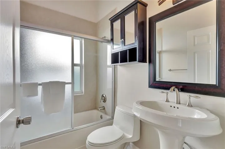 Full bathroom with toilet, enclosed tub / shower combo, and sink