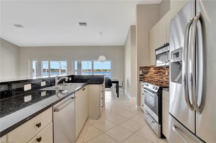 Kitchen with sink, hanging light fixtures, dark stone countertops, light tile patterned floors, and appliances with stainless steel finishes