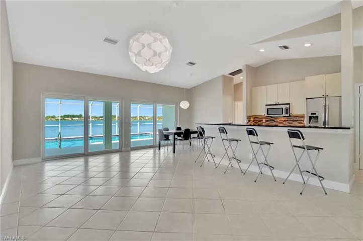 Kitchen with pendant lighting, white cabinets, appliances with stainless steel finishes, light tile patterned flooring, and a breakfast bar area