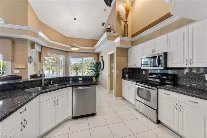 Kitchen with stainless steel appliances, sink, light tile patterned floors, a high ceiling, and white cabinetry