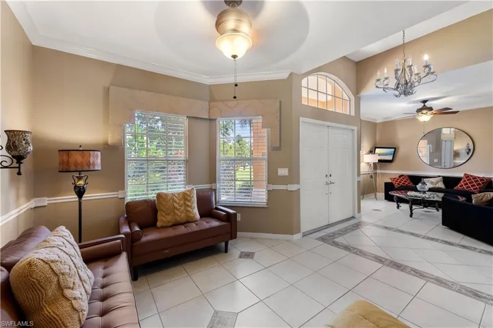 Living room featuring ceiling fan with notable chandelier, light tile patterned floors, and ornamental molding