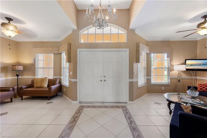 Entryway with crown molding, ceiling fan with notable chandelier, and light tile patterned floors