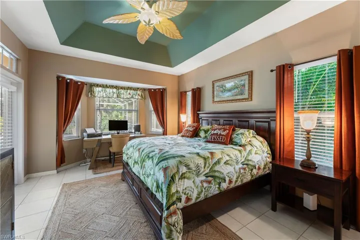 Bedroom with a tray ceiling, light tile patterned floors, and ceiling fan