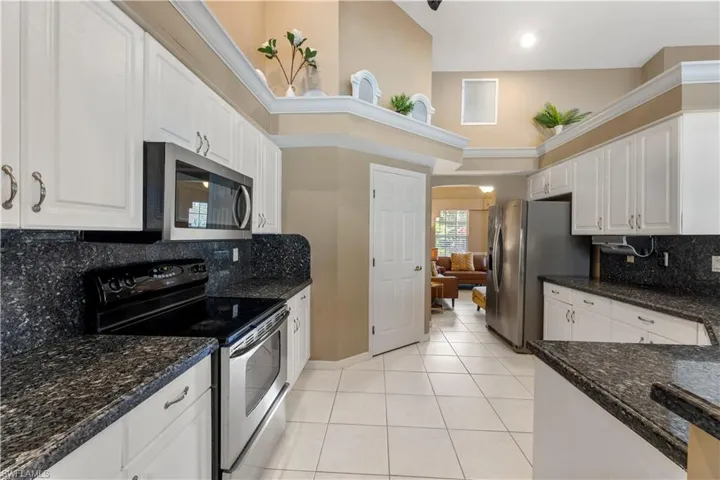 Kitchen featuring dark stone counters, stainless steel appliances, white cabinets, light tile patterned floors, and backsplash