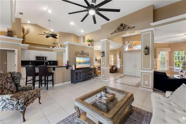 Tiled living room with decorative columns, ceiling fan, and high vaulted ceiling