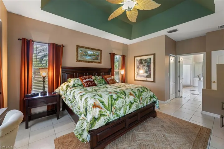 Bedroom featuring light tile patterned flooring, a raised ceiling, ensuite bathroom, and ceiling fan