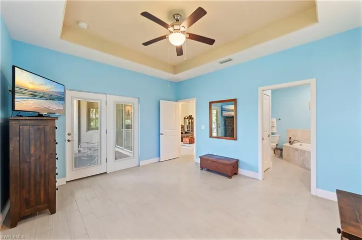 Bedroom with access to exterior, ceiling fan, a raised ceiling, light wood-style floors, and ensuite bath
