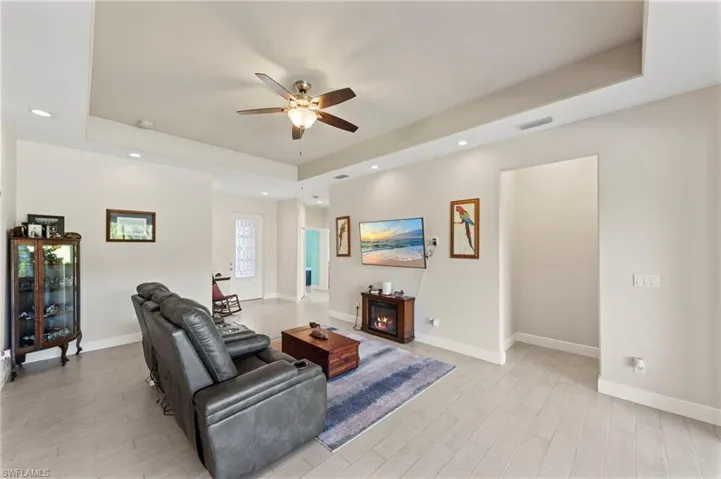 Living room with a raised ceiling, a ceiling fan, light wood-type flooring, recessed lighting, and a lit fireplace