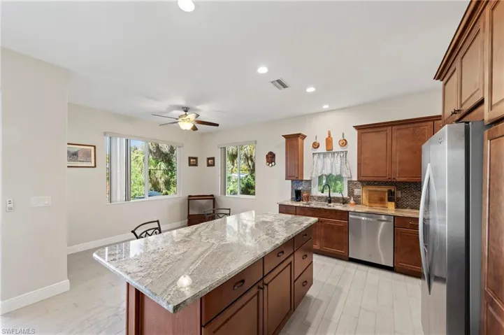 Kitchen featuring stainless steel appliances, a kitchen island, backsplash, light wood finished floors, and light stone countertops