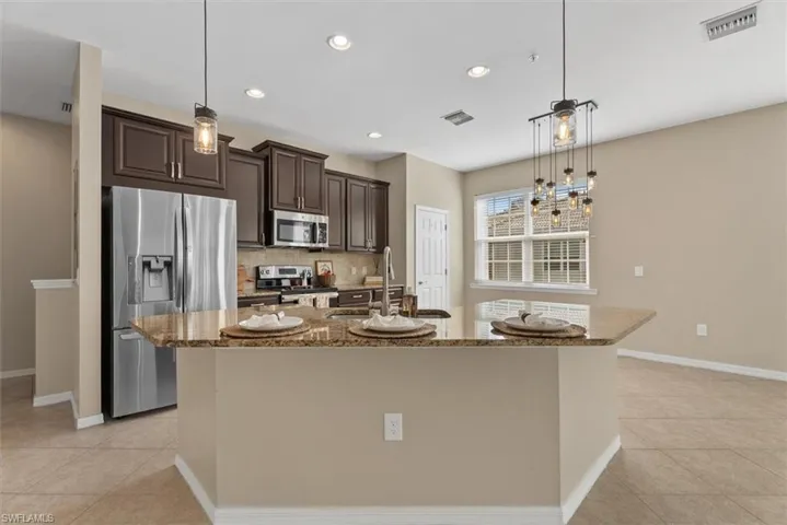 Kitchen featuring stainless steel appliances, dark wood-finish cabinetry, a large island with a stone-finish countertop, and recessed lighting