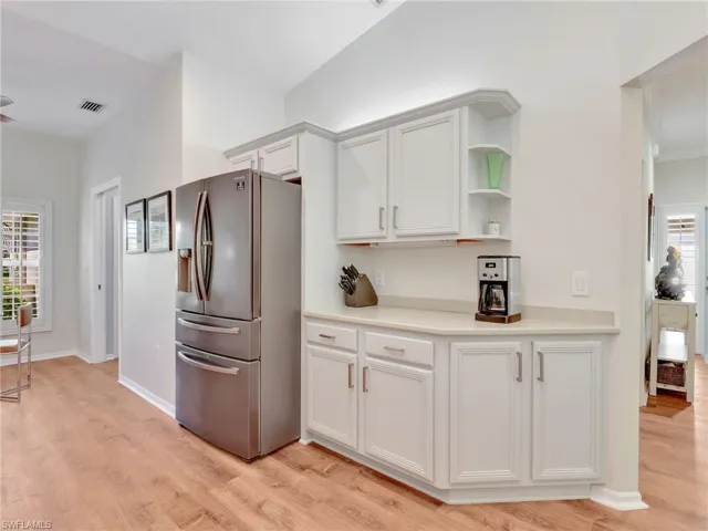 Kitchen with stainless steel fridge, white cabinets, light wood-style flooring, and open shelves