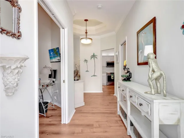 Hallway featuring a tray ceiling, light wood-style floors, and crown molding