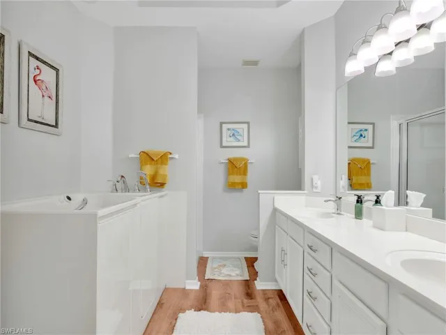 Bathroom with double vanity, a garden tub, light wood finished floors, and a shower with door