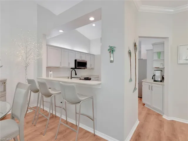 Kitchen with a breakfast bar area, light wood finished floors, white cabinets, appliances with stainless steel finishes, and recessed lighting