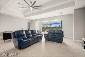 Living room featuring a raised ceiling, light tile patterned floors, and ceiling fan