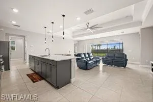 Kitchen with light countertops, open floor plan, a ceiling fan, hanging light fixtures, and a kitchen island with sink