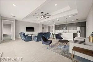 Living room with a tray ceiling, ceiling fan, recessed lighting, and light tile patterned floors