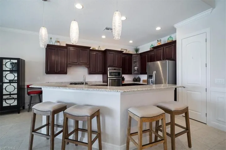 Kitchen with stainless steel appliances, ornamental molding, a center island with sink, and pendant lighting