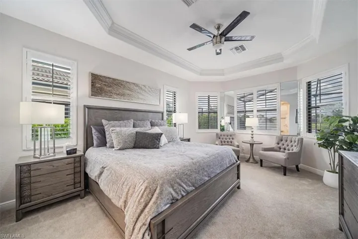 Carpeted bedroom featuring ceiling fan, a raised ceiling, and crown molding