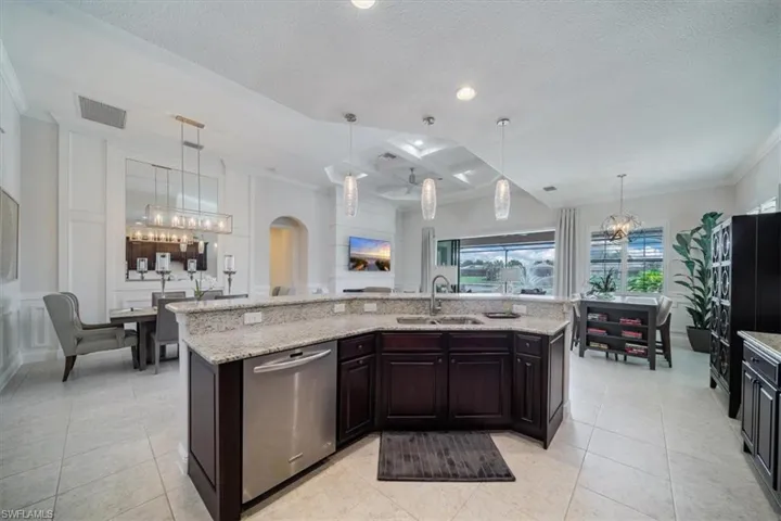 Kitchen with sink, light stone countertops, a center island with sink, and stainless steel dishwasher