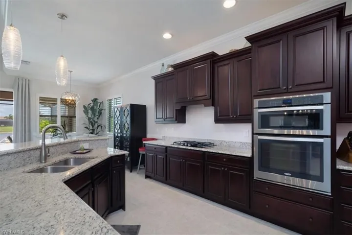 Kitchen featuring light tile flooring, crown molding, appliances with stainless steel finishes, sink, and pendant lighting