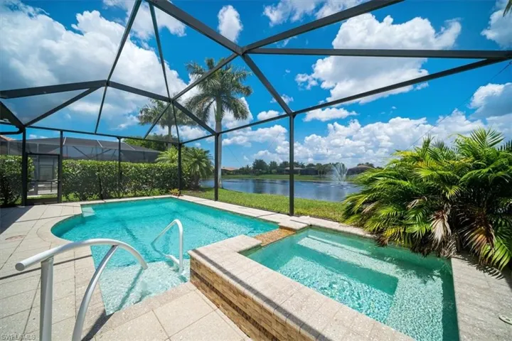 View of pool featuring a patio, glass enclosure, an in ground hot tub, and a water view