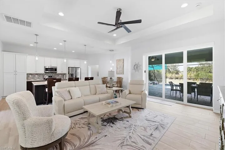 Living area with a raised ceiling, a ceiling fan, light wood-style floors, and recessed lighting