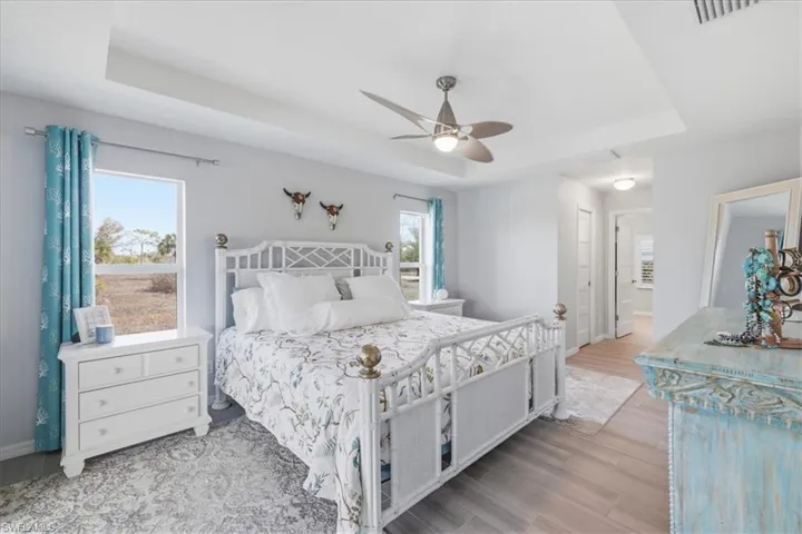 Bedroom with a tray ceiling, light wood-style flooring, a ceiling fan, a closet, and ensuite bathroom