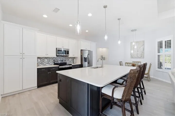 Two tone kitchen featuring two tone cabinets, a breakfast bar area, stainless steel appliances, tasteful backsplash, and light wood-style floors
