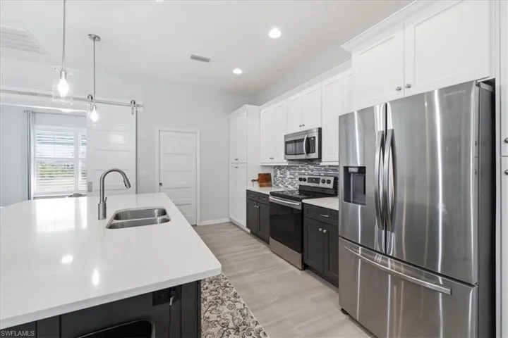 Dual tone kitchen with stainless steel appliances, two tone cabinets, decorative light fixtures, decorative backsplash, and light wood finished floors