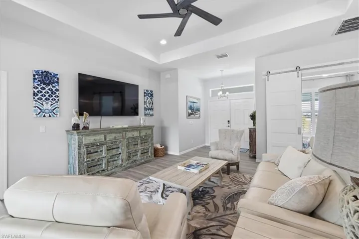 Living area with a tray ceiling, a barn door, ceiling fan, wood finished floors, and suspended lighting