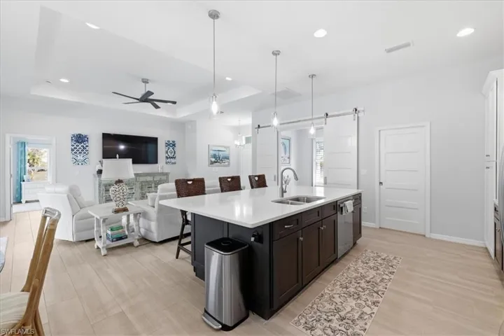 Kitchen with a barn door, a breakfast bar area, a raised ceiling, a center island with sink, and pendant lighting