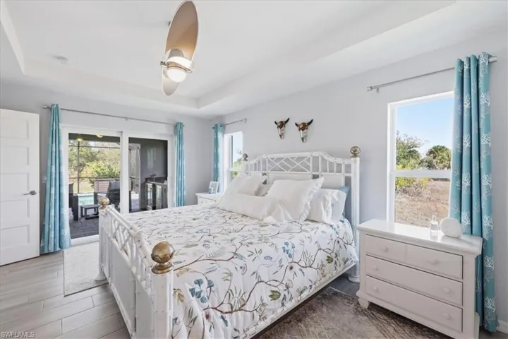Bedroom with access to outside, a raised ceiling, wood finished floors, and ceiling fan
