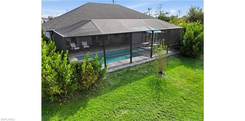 Back of property featuring an outdoor pool, a lanai, a yard, and a shingled roof