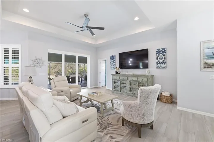 Living room with a ceiling fan, light wood-style floors, a raised ceiling, and recessed lighting