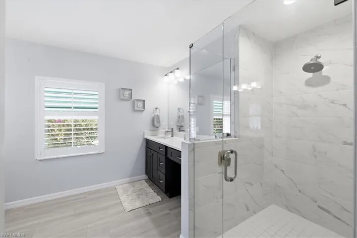 Full bath with a marble finish shower, double vanity, and light wood-style floors