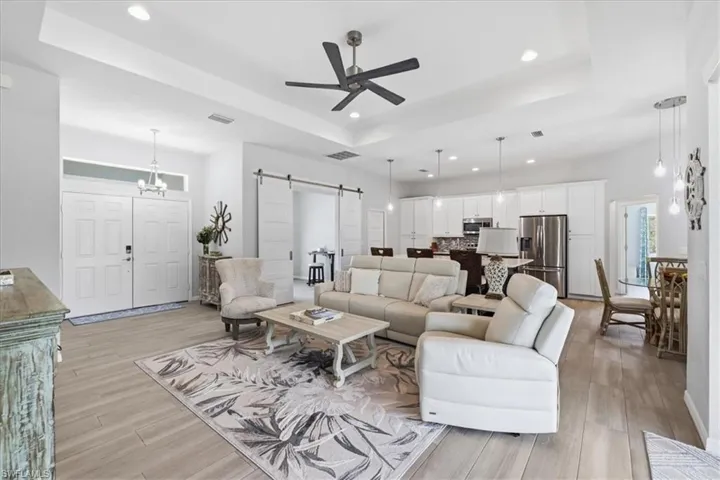 Living area featuring a barn door, ceiling fan, a raised ceiling, light wood-style flooring, and a chandelier