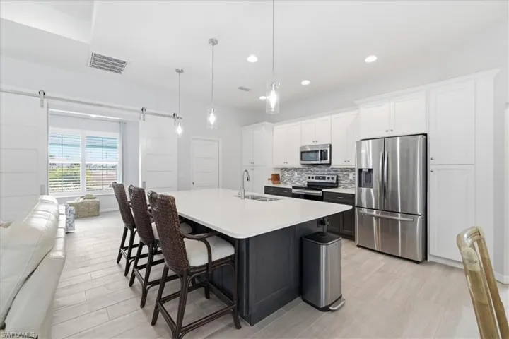 Two tone kitchen with two tone cabinetry, stainless steel appliances, a breakfast bar, a kitchen island with sink, and a barn door