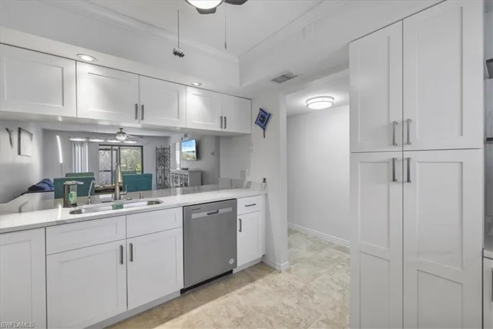 Kitchen with a ceiling fan, white cabinets, open floor plan, stainless steel dishwasher, and crown molding
