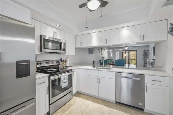 Kitchen featuring a ceiling fan, appliances with stainless steel finishes, white cabinets, ornamental molding, and a raised ceiling