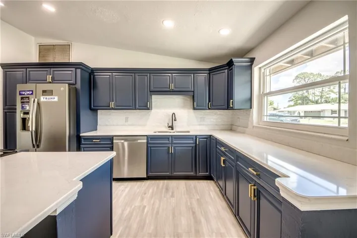 Kitchen with appliances with stainless steel finishes, vaulted ceiling, decorative backsplash, light wood-type flooring, and blue cabinets