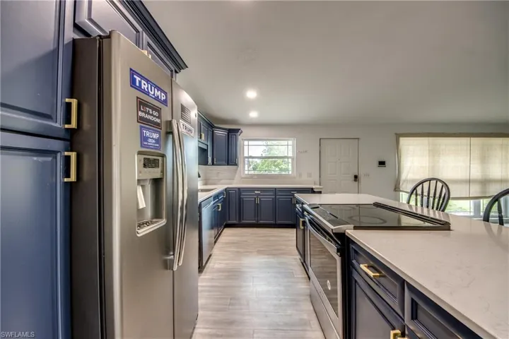 Kitchen with appliances with stainless steel finishes, light wood-style flooring, blue cabinets, light stone countertops, and recessed lighting