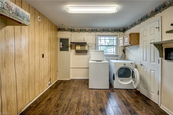 Laundry room featuring washer and clothes dryer, electric panel, dark wood finished floors, cabinet space, and wooden walls