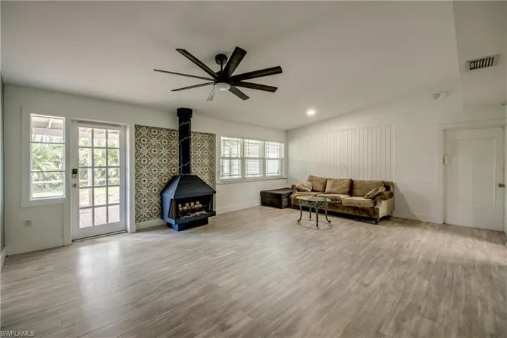 Living area featuring a wood stove, ceiling fan, vaulted ceiling, and wood finished floors